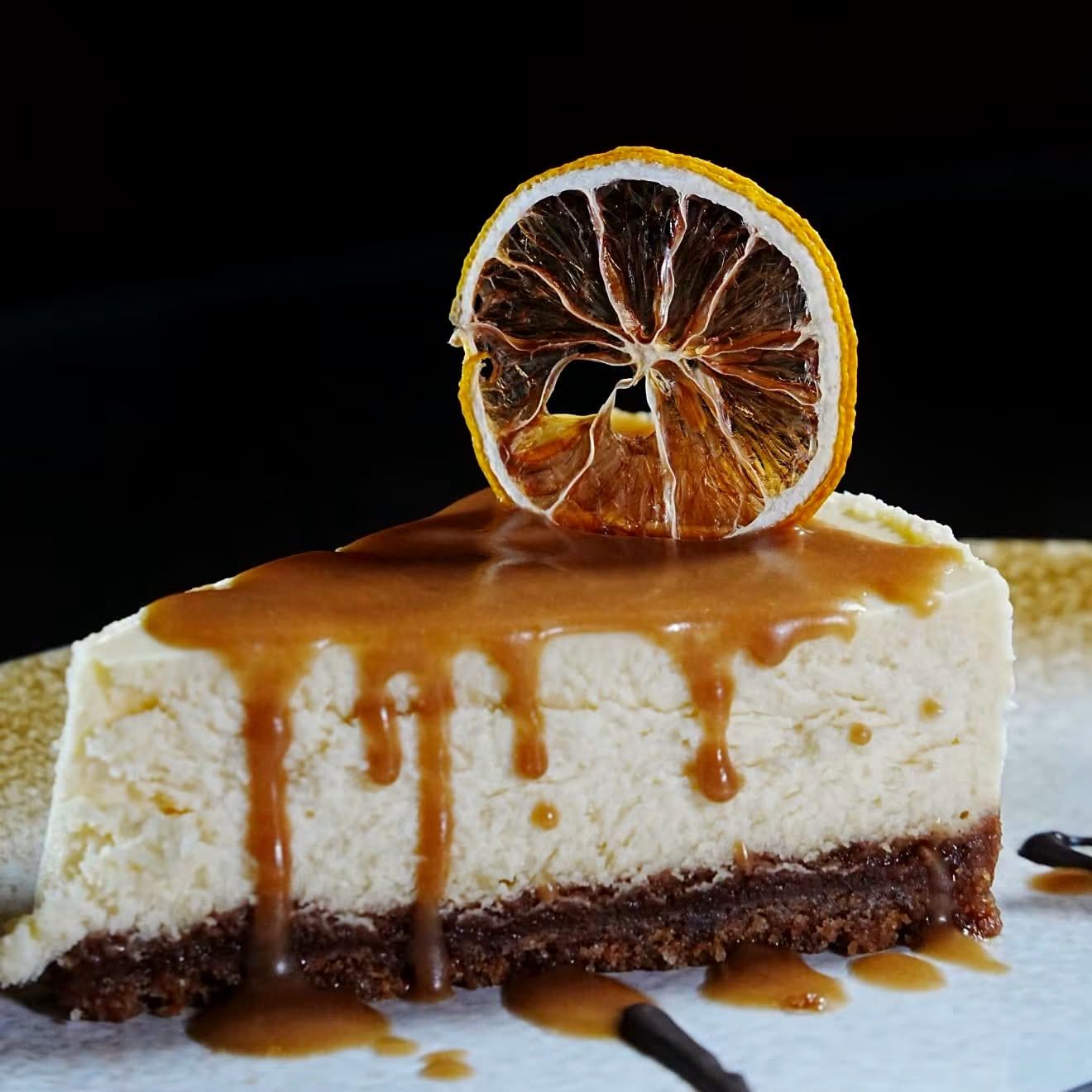 A slice of cheesecake with caramel sauce and a dried orange slice