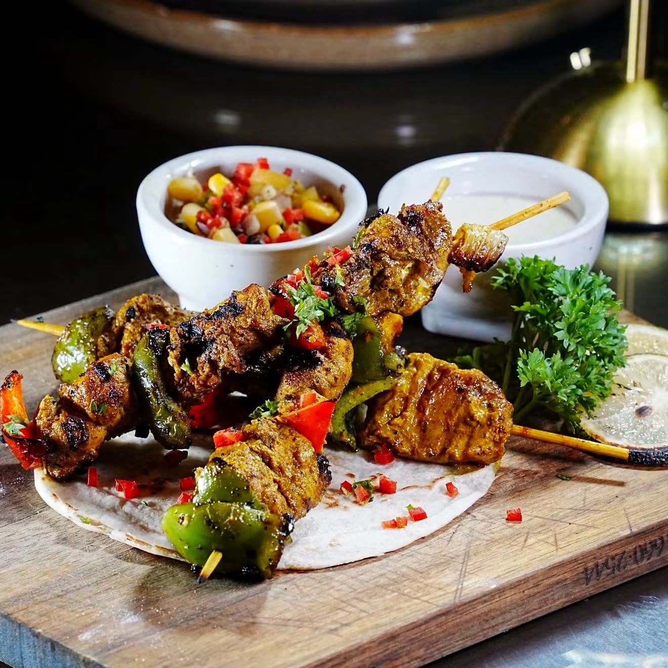 Grilled chicken skewers with peppers and onions, a salsa and a creamy dip on a wooden board