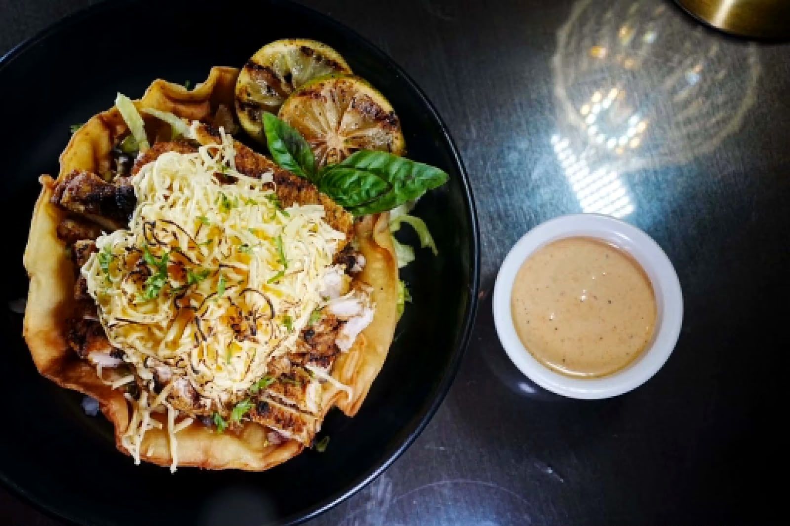 A salad in a crispy tortilla bowl with a dipping sauce