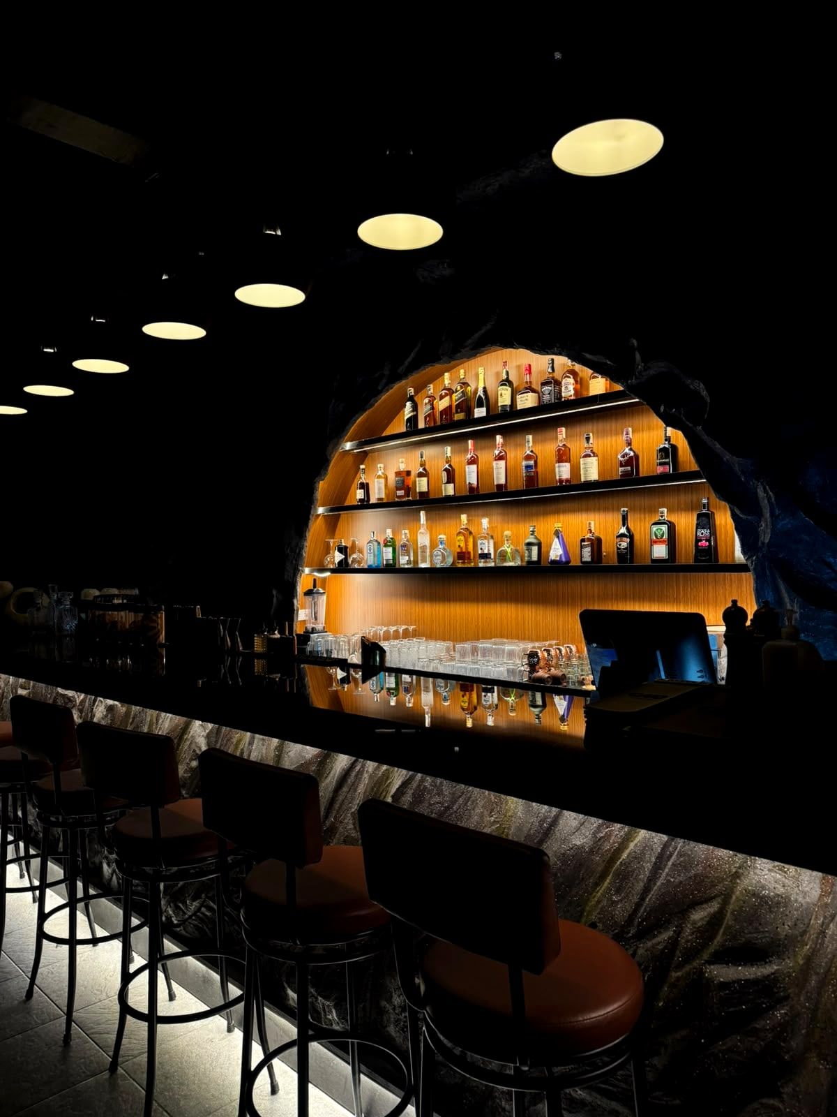 The arched bar at night: glowing bottle shelves inside the rock, with bar stools along the counter