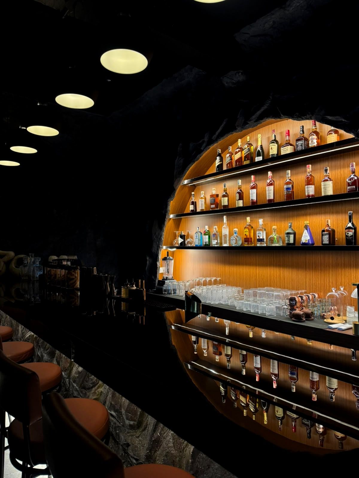 The arched bar at night, its glowing bottle shelves reflected in the dark counter