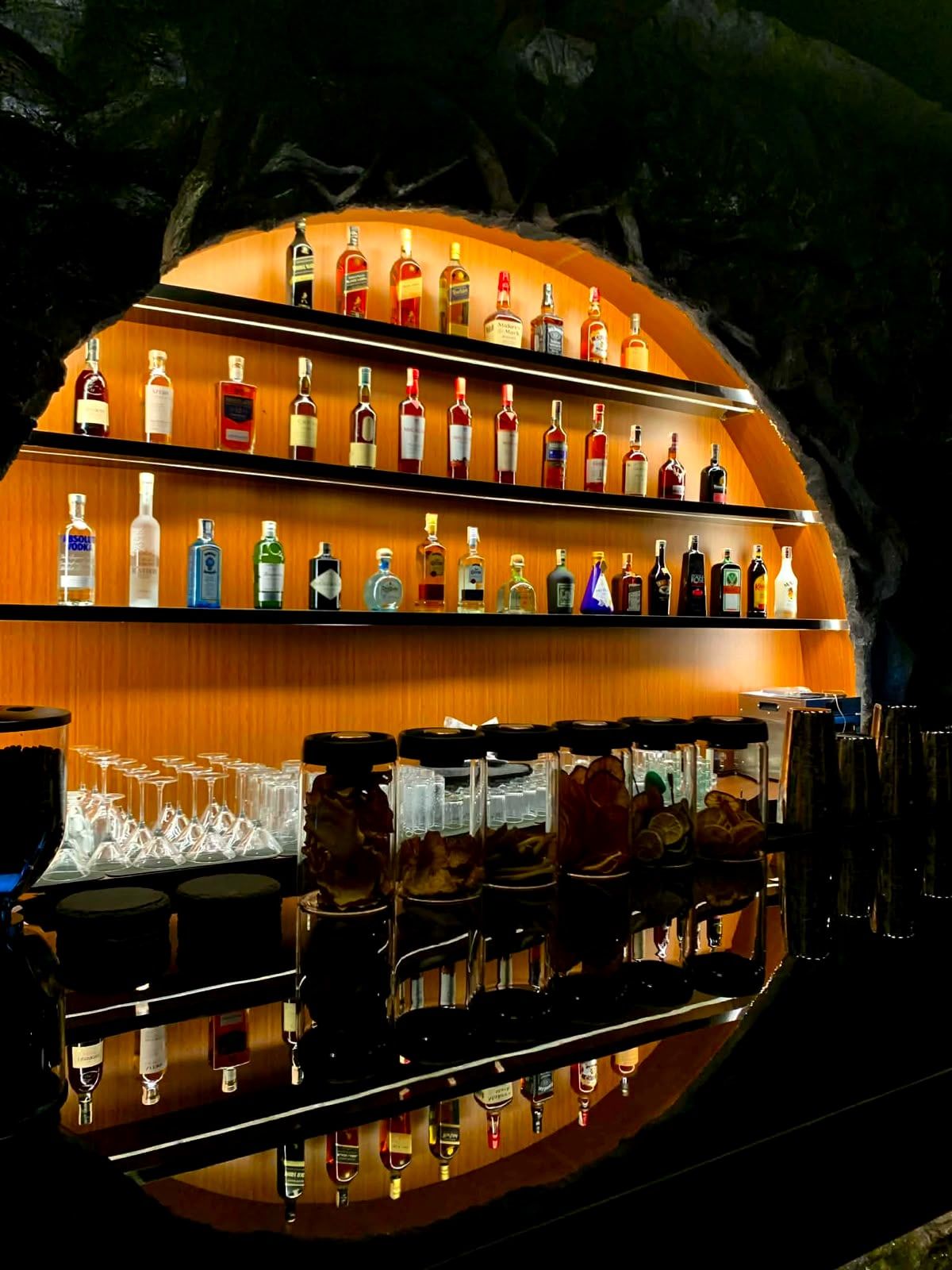 Bottle shelves glowing amber inside a round stone arch at Cavo