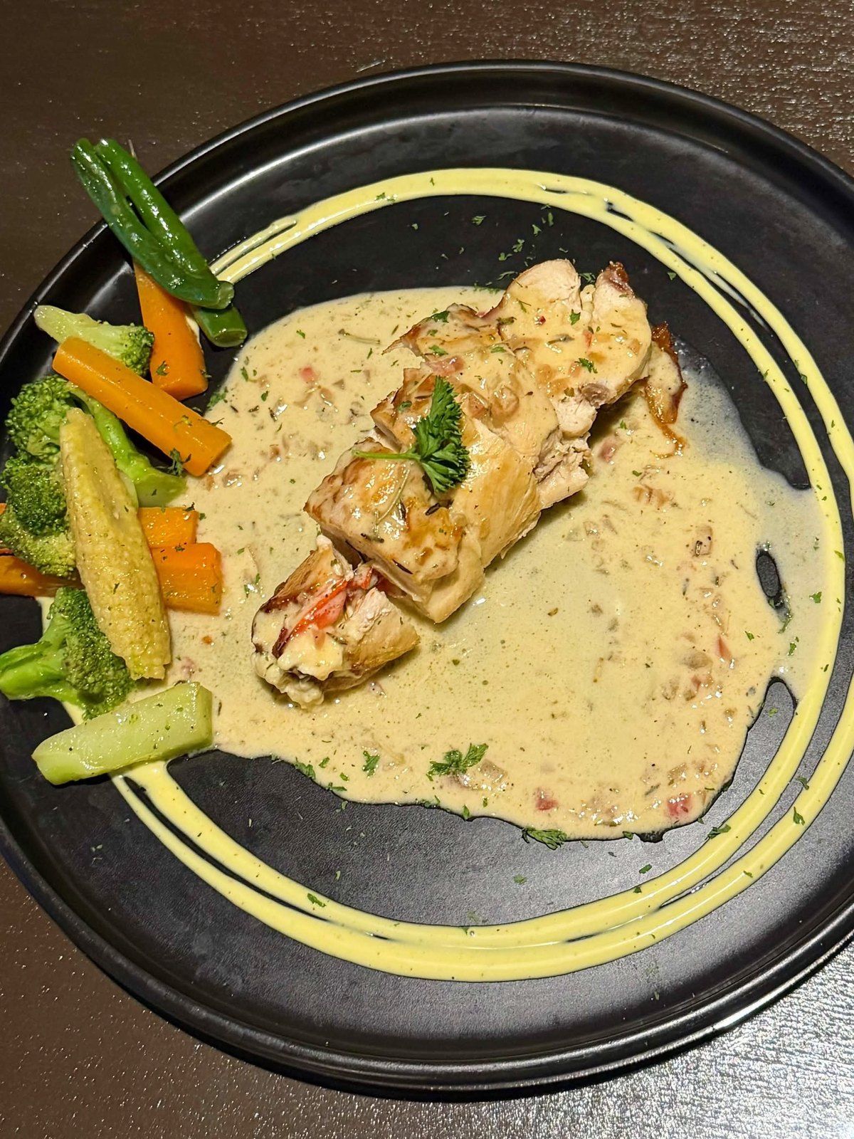 Chicken roulade in cream sauce with grilled vegetables on a black plate