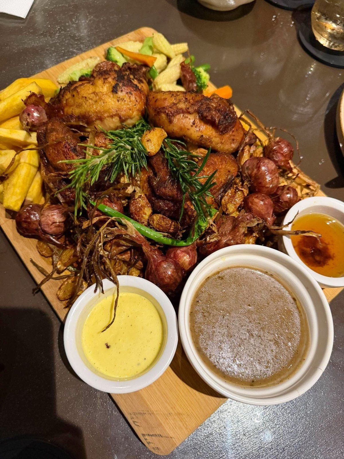 A roast chicken platter with potatoes and dipping sauces on a wooden board
