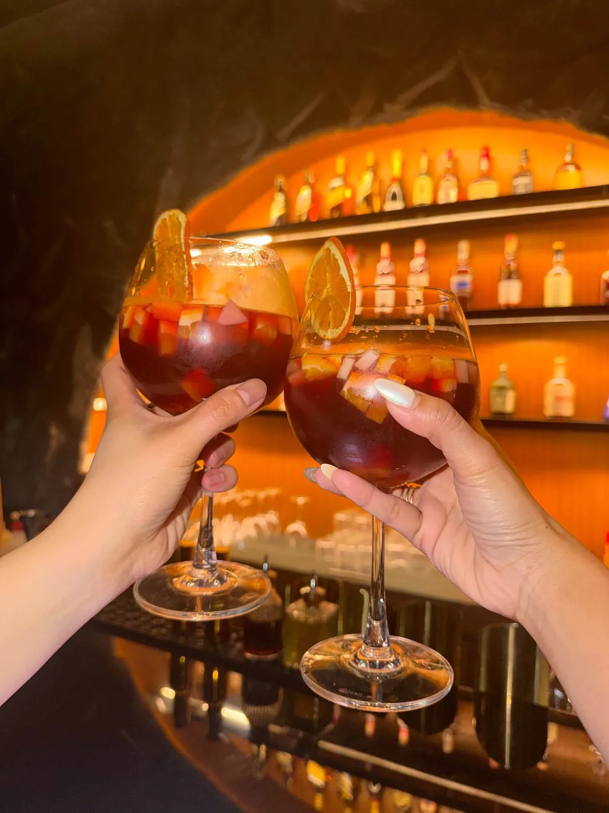 Two guests clink glasses of sangria in front of the glowing arched bar at Cavo