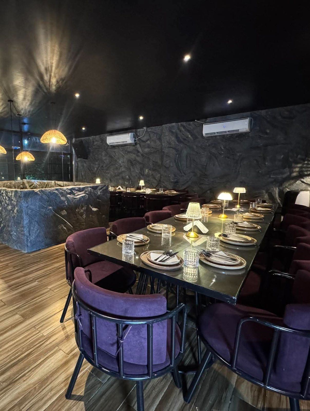The upper floor set for dinner, with purple chairs, rock walls and woven pendant lights