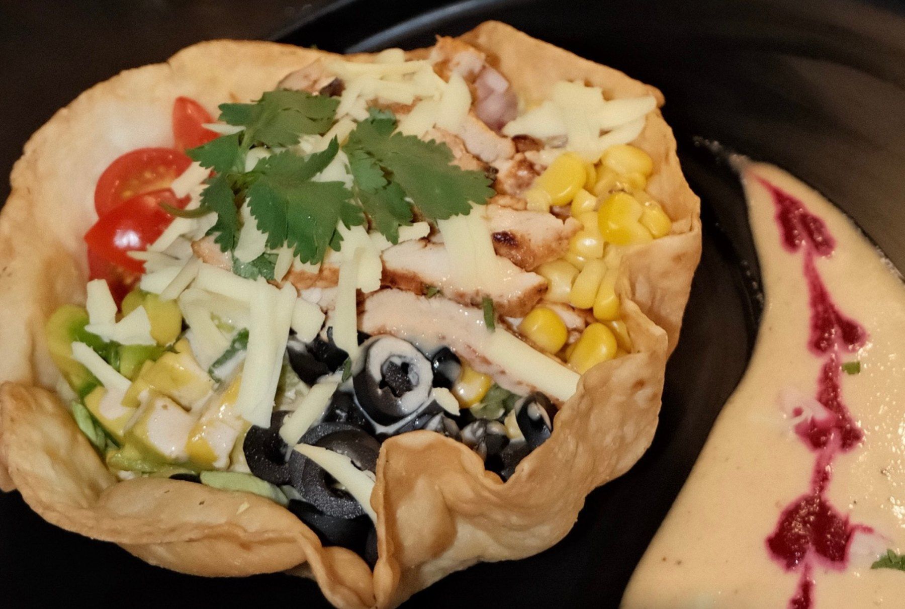 A taco salad with chicken, corn, cheese and cherry tomatoes in a crisp tortilla bowl