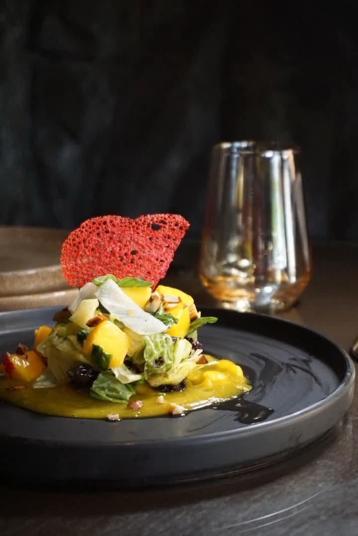 Greens and mango on a yellow sauce, topped with a red lace tuile