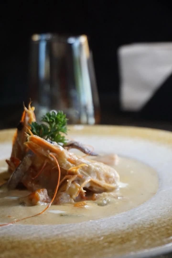 A whole prawn on a pool of cream sauce, served on a white plate in warm light