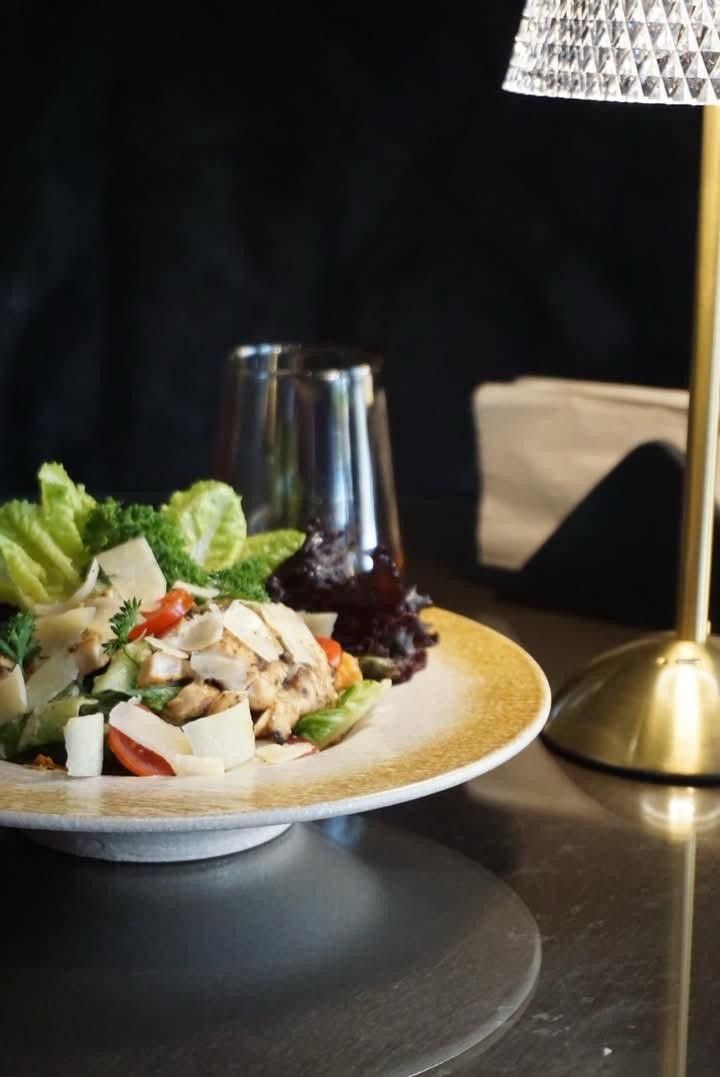 A green salad with chicken and tomato on a gold rimmed white plate