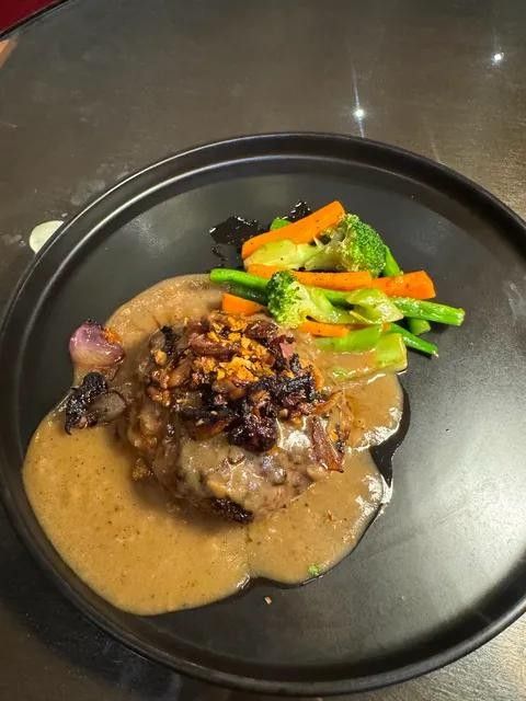 A beef patty in gravy with caramelized onions and vegetables