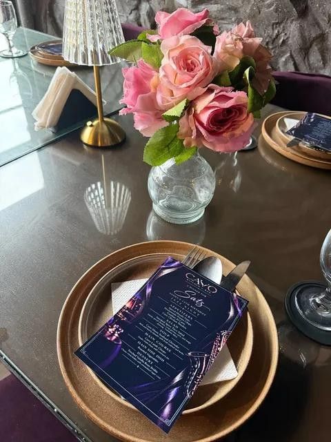 A table set with pink roses, a gold charger and a Cavo menu card