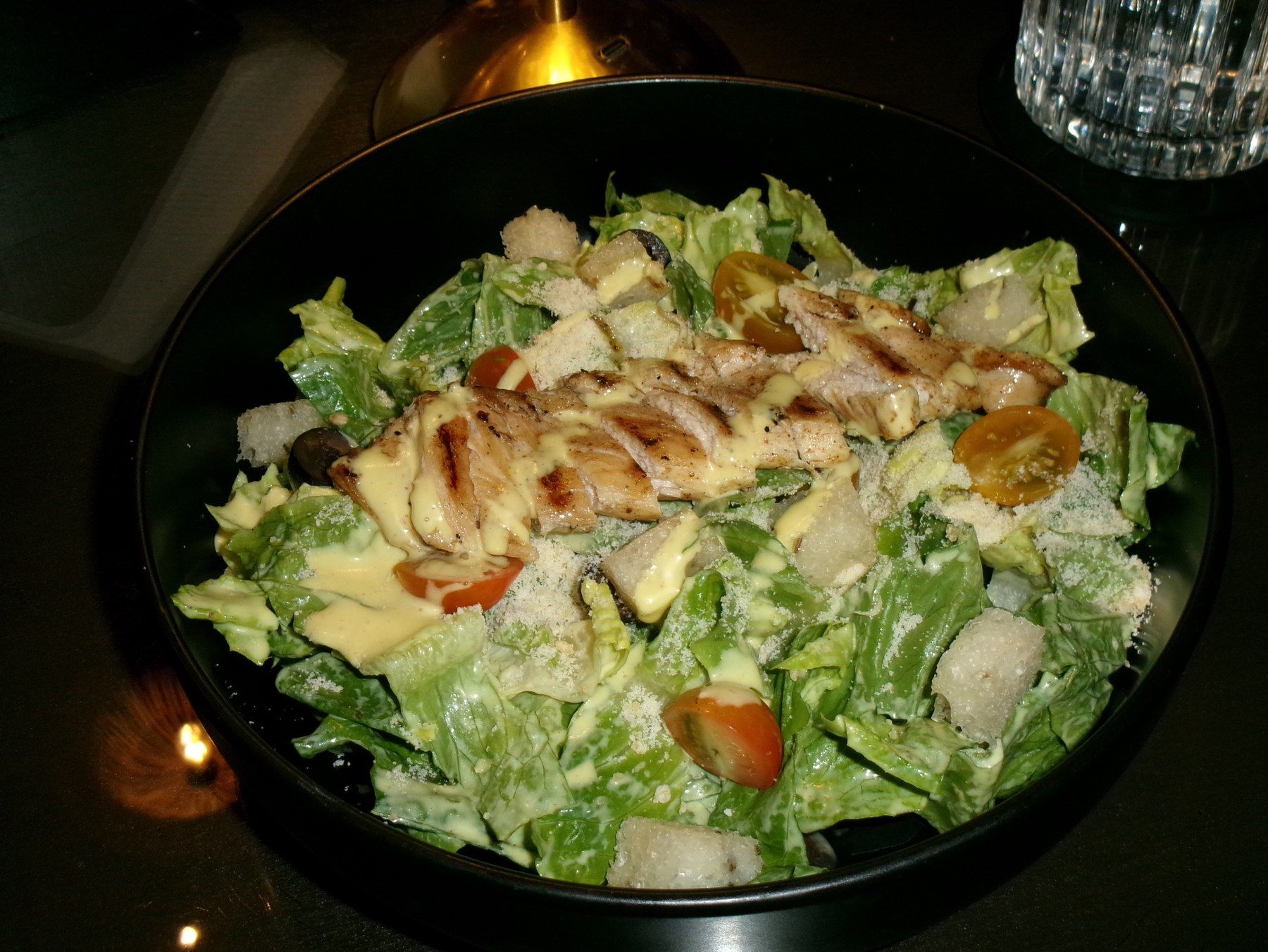 Grilled chicken Caesar salad with croutons and cherry tomatoes in a black bowl