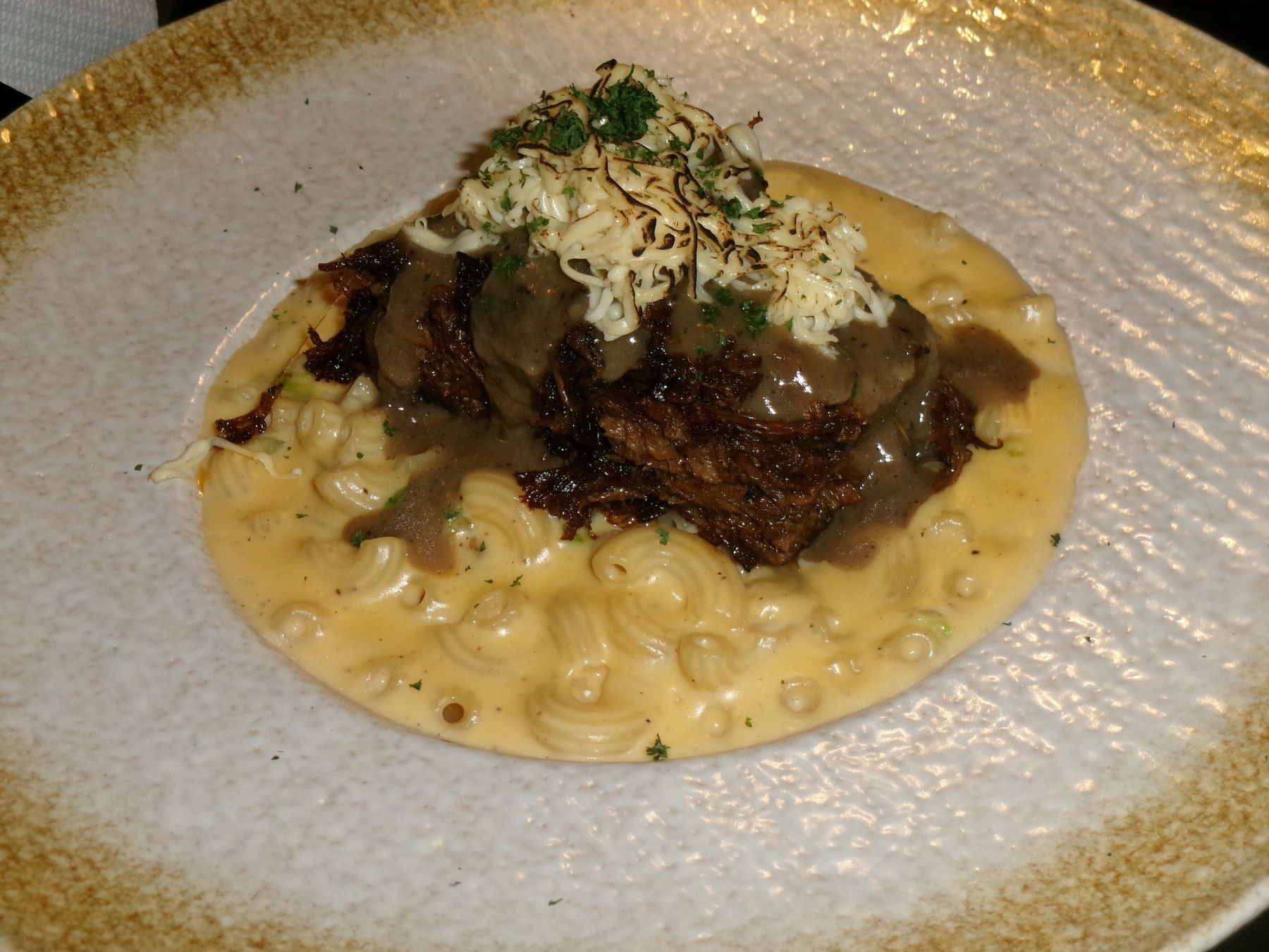 Braised short rib on creamy mac and cheese in a gold rimmed bowl